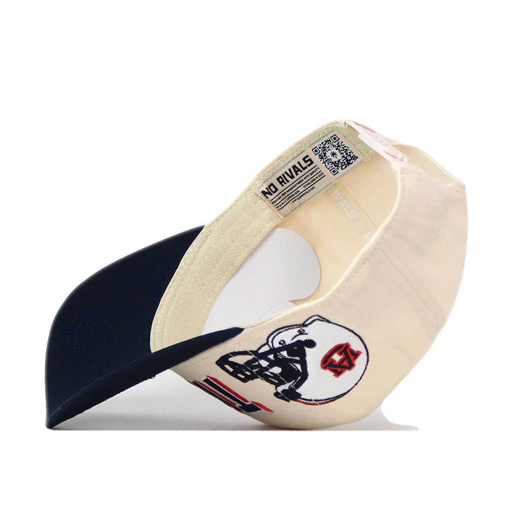 The No Rivals Auburn Alma Mater Hat, a cream and navy snapback, is shown upside down to highlight its interior label and QR code, while the front features an embroidered football helmet graphic—making it the perfect finishing touch for your gameday look.
