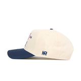 Side view of the No Rivals Florida Gators 250th Americana Hat, cream-colored with a navy blue brim, featuring embroidered NR initials above the brim and a snapback closure for adjustable fit.