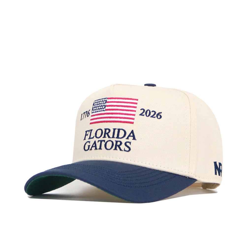 The Florida Gators 250th Americana Hat by No Rivals is a beige and navy snapback with an embroidered American flag, 1776, 2026, Florida Gators on the front, and features an official logo plus "NF" on the brim.