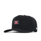 The Nebraska Cornhuskers Trainer Hat by No Rivals is a black snapback cap featuring a bold red N rubberized logo on the front and a small NR tag on the side, shown against a white background—perfect for your gameday fit.