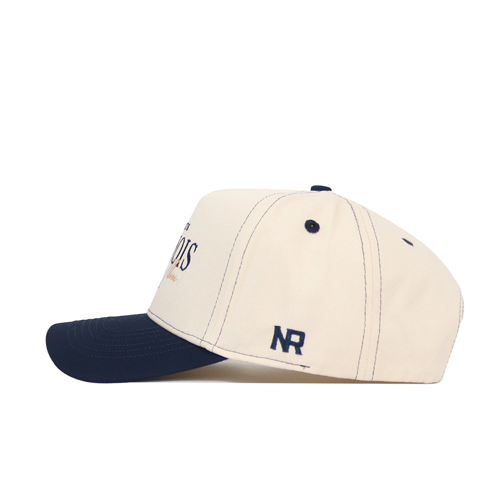 The University of Illinois Vintage Hat by No Rivals is a beige snapback with a navy brim, button, and dark blue stitching. "NR" is embroidered on the side. Made from premium cotton, the structured cap is displayed in side profile on a white background.