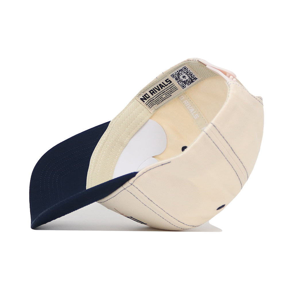 The University of Illinois Vintage Hat by No Rivals is shown upside down, revealing its inner lining, stitching, and a QR code label. This structured beige cap with a dark blue brim is crafted from high quality cotton for lasting comfort.