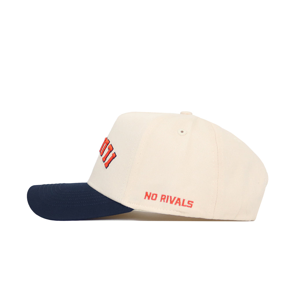The Upside Down Illinois Hat by No Rivals is a cream cotton baseball cap with a navy blue brim and “NO RIVALS” embroidered in red on the side.