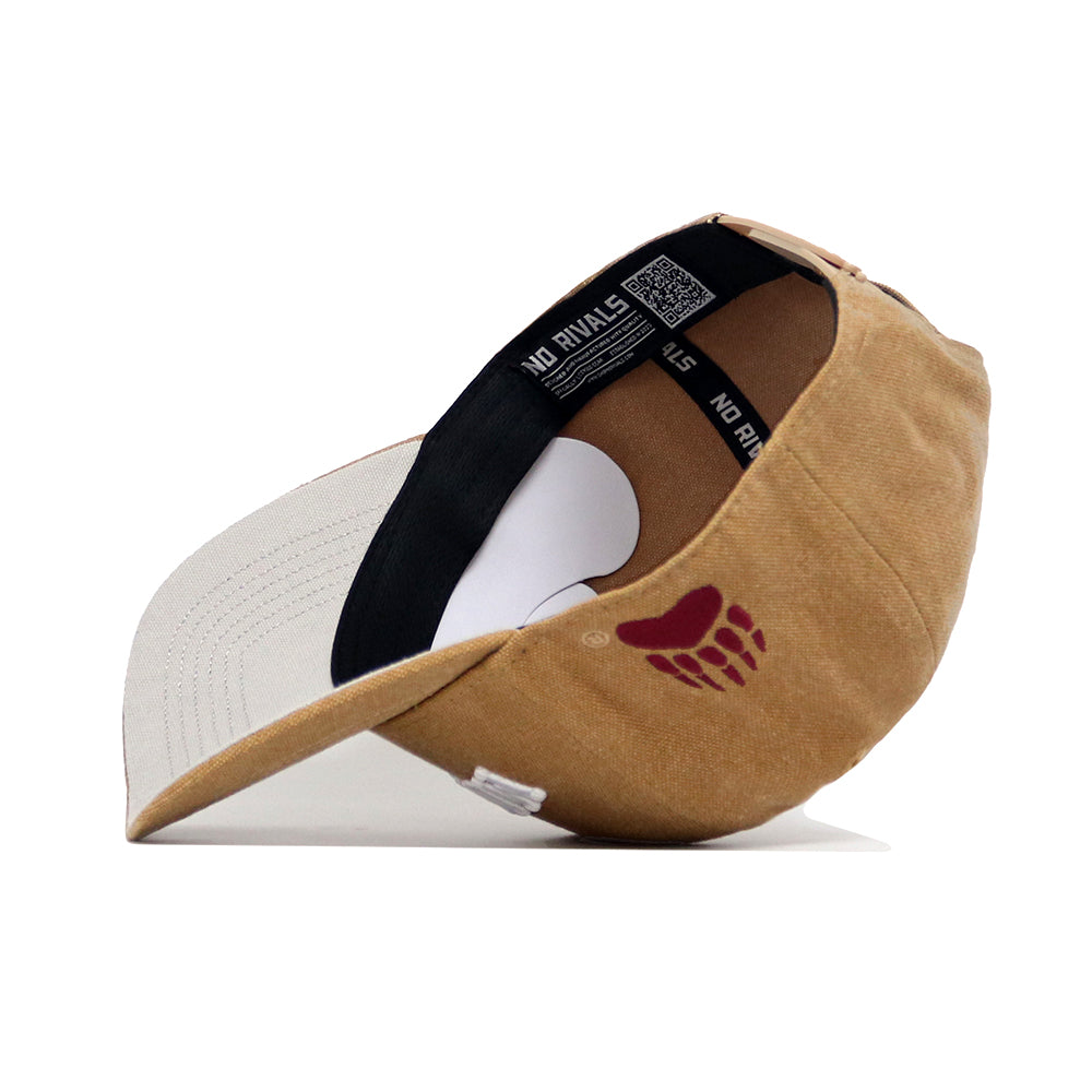 The Montana Rustic Hat by No Rivals is a tan and beige cotton canvas snapback, shown on its side with a black inner band featuring "NO RIVALS" text and a red paw print logo on the outer side for a structured fit.