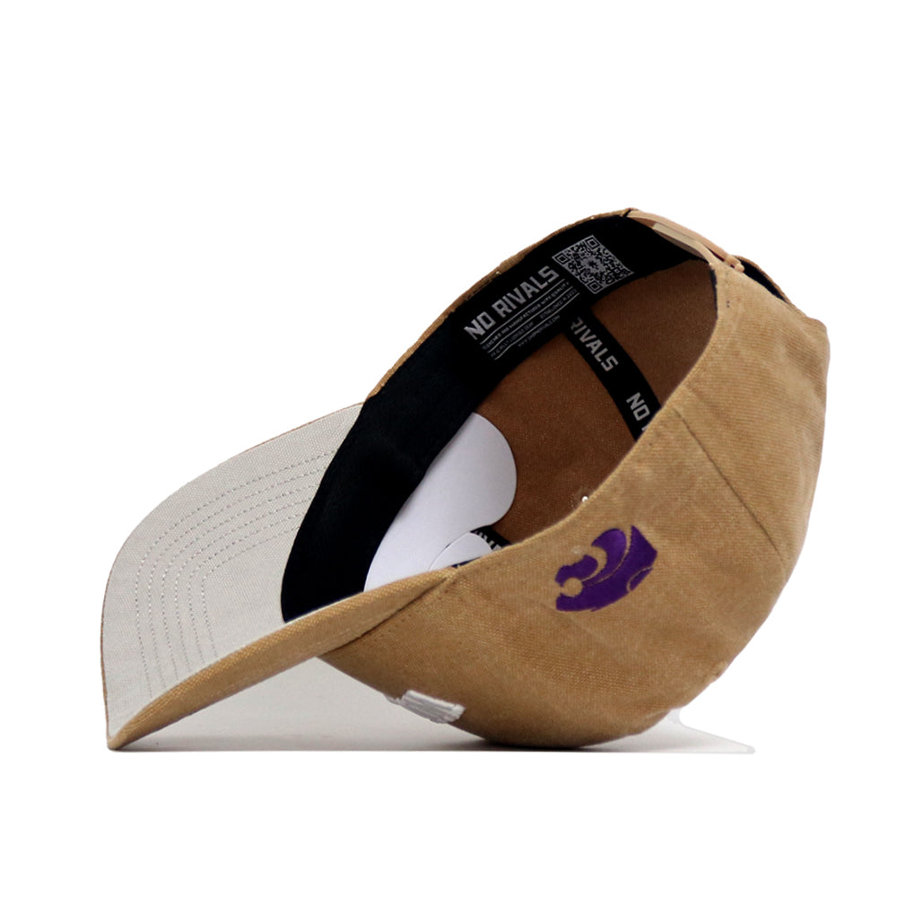The Kansas State Rustic Hat by No Rivals is a tan cotton canvas baseball cap with a curved brim, black NO RIVALS inner band, a small purple logo on the side, and visible interior details. Shown upside down.
