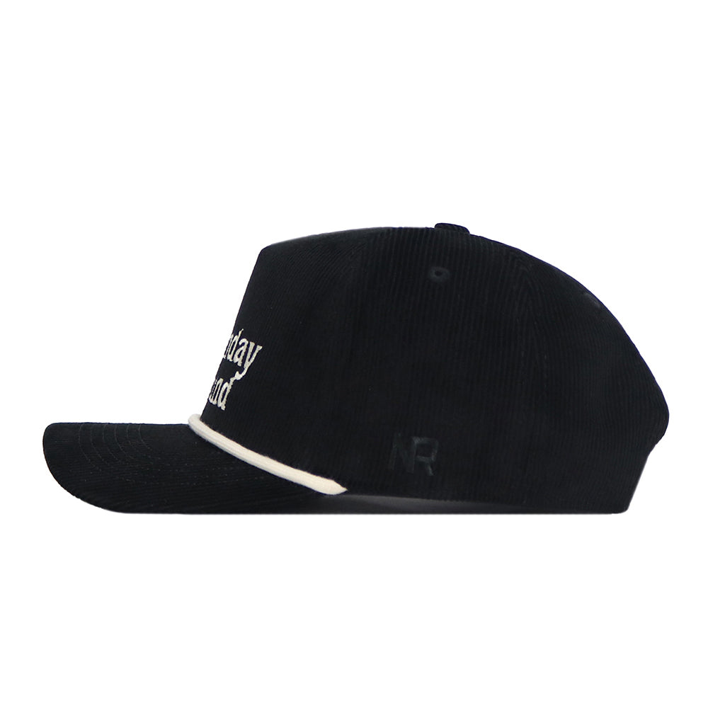 The No Rivals Sunday Round Cord Hat in black features cotton corduroy, white embroidered front text, a white trim above the curved brim, subtle side NR logos, and a snapback closure. Shown in a side profile view.