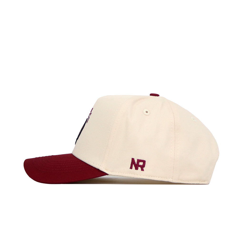 The No Rivals Montana Logo Patch Hat features a cream-colored snapback design with a maroon brim and a small maroon NR initials patch on the side. Made from high-quality cotton blend, it's displayed in side profile against a white background.