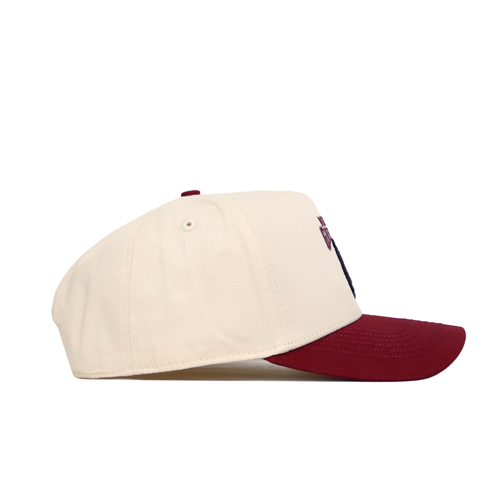 A side view of the No Rivals Montana Logo Patch Hat, featuring a cream crown and maroon brim in high-quality cotton blend, shown on a white background.