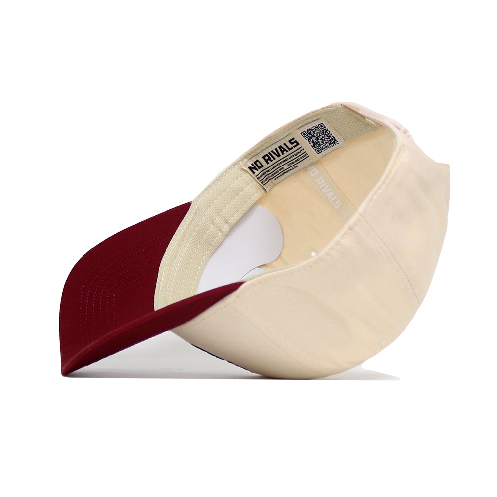 The Montana Logo Patch Hat by No Rivals is shown from underneath, displaying inner labels, stitching, printed text, and a QR code on the inside band. It features a beige crown with maroon brim and is crafted from a high quality cotton blend.