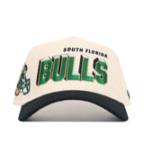 A cream and black snapback from the USF Alma Mater Collection by No Rivals, featuring "South Florida Bulls" embroidered in green, black, and gold and a bull mascot detail. Made from high-quality cotton and officially licensed for true fans.