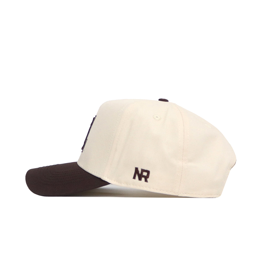 The No Rivals Arizona Espresso Hat is a cream-colored baseball cap with a dark brown brim. Made from high quality cotton, this structured hat has "NR" embroidered in brown on the side near the back.