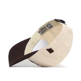 The No Rivals Arizona Espresso Hat is a cream and brown high-quality cotton baseball cap, shown inside at an angle with a dark brown brim, fabric strap, and care label featuring text and a QR code on the inner band.