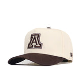The Arizona Espresso Hat by No Rivals is a beige snapback with a brown brim and a bold, dark brown A logo outlined in white on the front, plus NR branding on the side. Made from premium cotton and officially licensed.