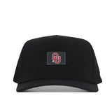 The Oklahoma Sooners Trainer Hat by No Rivals is a black snapback crafted from high-quality cotton with a structured fit, and features a rectangular patch on the front displaying the red OU logo for the University of Oklahoma.