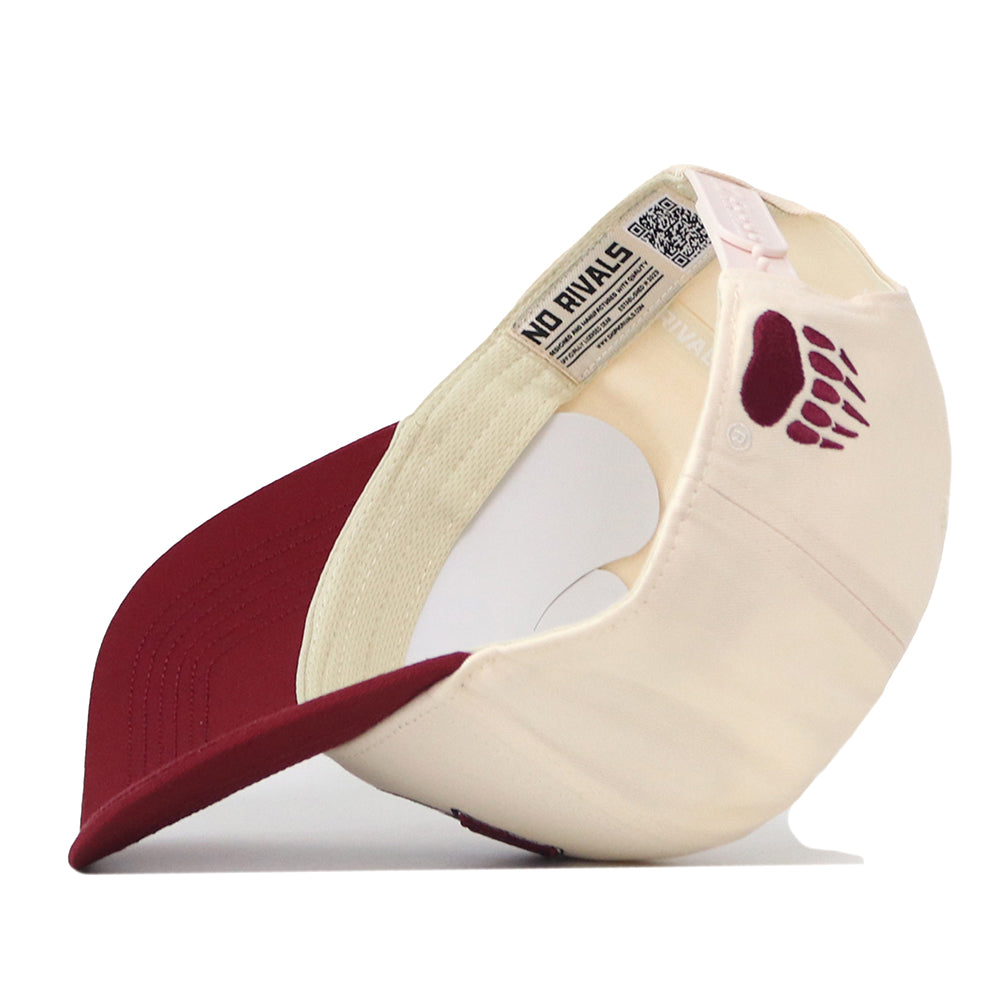 A cream and maroon Montana Grizzlies Stadium Hat by No Rivals is flipped inside out, revealing an embroidered paw print logo on the side, a QR code on the inner tag, and the brand name “No Rivals” printed inside.