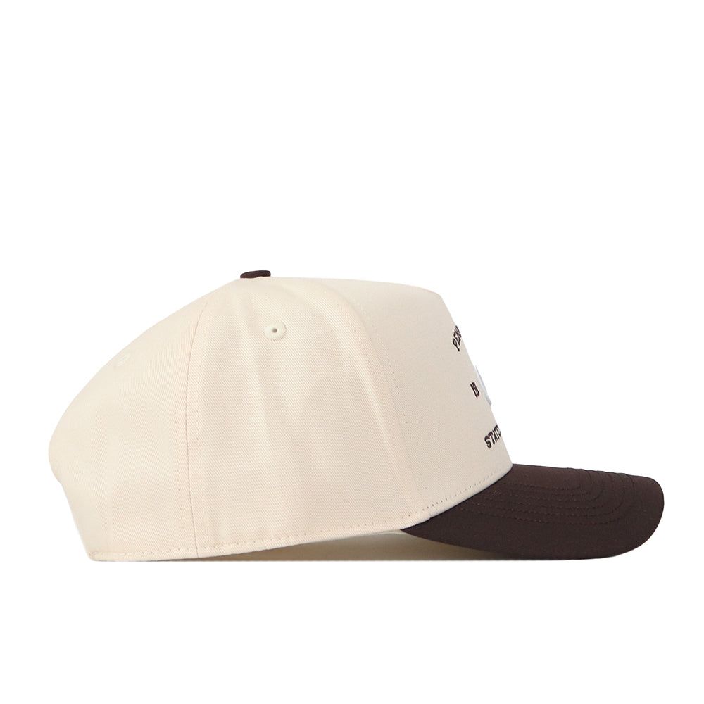 The No Rivals Penn State Outlaw Hat - Classic is a beige baseball cap with a dark brown brim, shown from the side on a white background. It features a snapback adjustment for the perfect gameday fit.