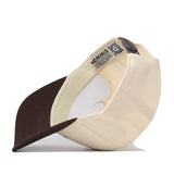 A cream and brown Penn State Outlaw Hat - Classic by No Rivals lies on its side, displaying the inside label reading “NO RIVALS” and a visible QR code tag near the adjustable snap back strap.