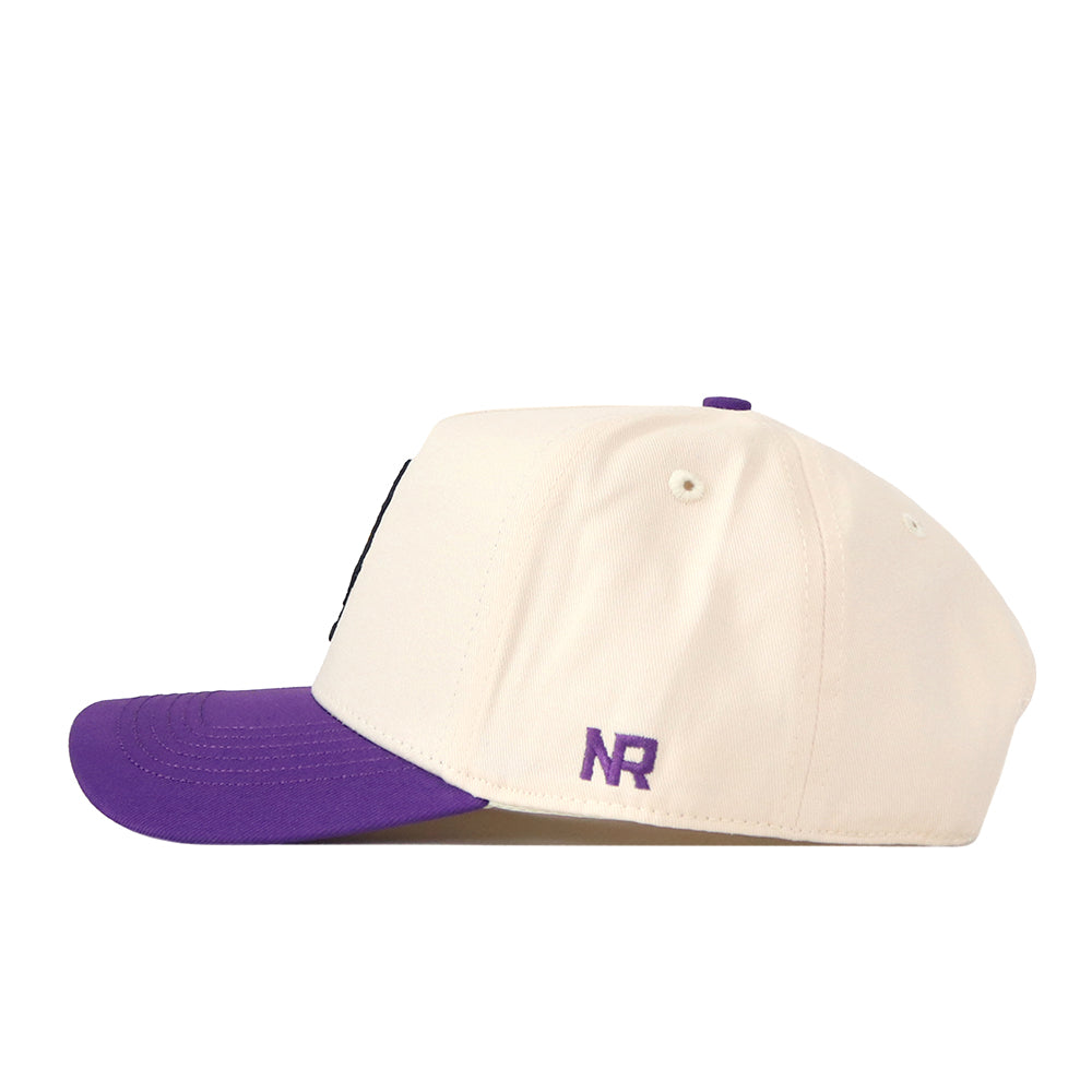 The ECU Vintage Patch Hat by No Rivals is a white snapback cap with a purple bill, displayed from a side angle. The letters NR are embroidered in purple near the back, making it an ideal accessory for any gameday outfit.