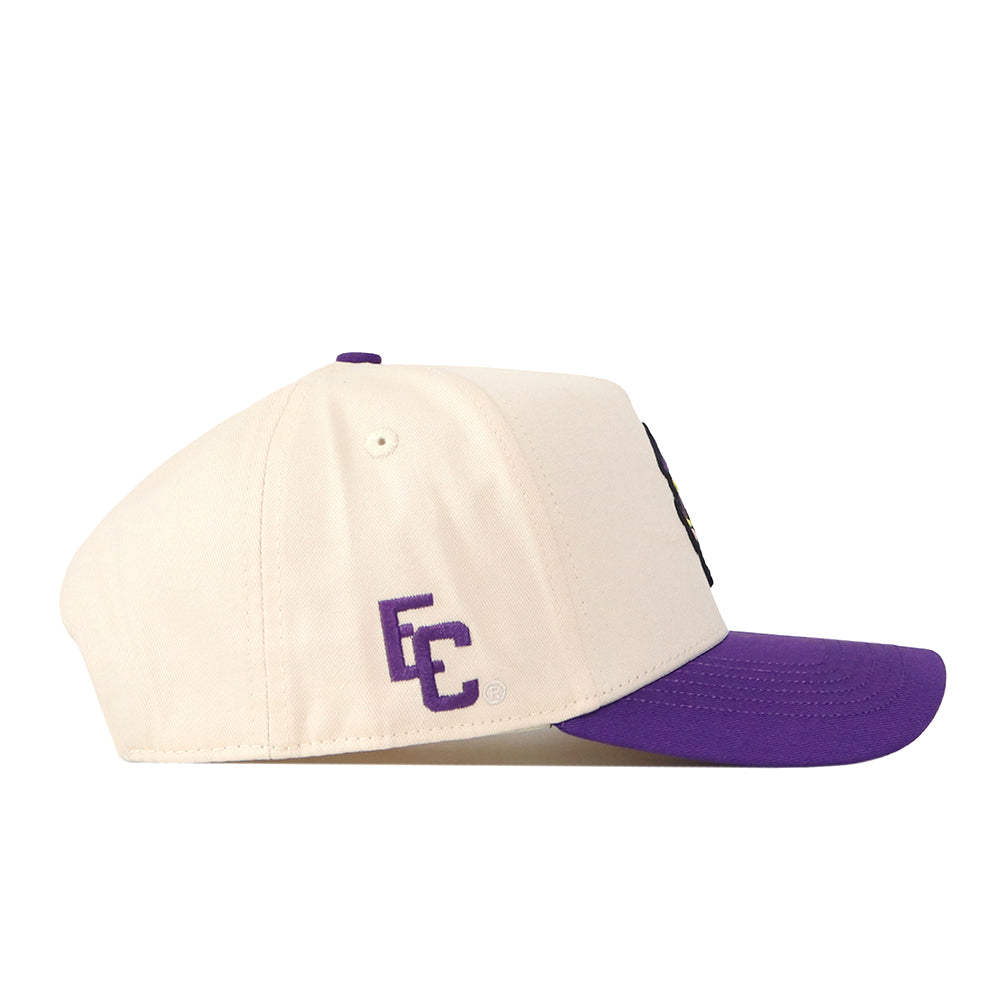 Introducing the ECU Vintage Patch Hat by No Rivals—a cream-colored snapback with a purple brim and “EC” embroidered in purple on the side, featuring crisp embroidered logos. Shown in profile view against a white background, it’s the perfect finishing touch for your next Gameday fit.
