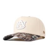 Show off your gameday style with the Auburn Camo Connector Hat by No Rivals. This beige snapback features a white AU embroidered logo on the front and a camo-patterned brim, while a small gold emblem accents the side for an extra touch of flair. The hat is displayed at an angle against a white background.
