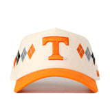 The Tennessee Argyle Hat by No Rivals is a cream and orange baseball cap showcasing an orange embroidered T logo on the front. Crafted from a high-quality cotton blend, it features an argyle pattern of orange, gray, and black diamonds on the sides and is finished with a snap back closure for adjustable comfort.