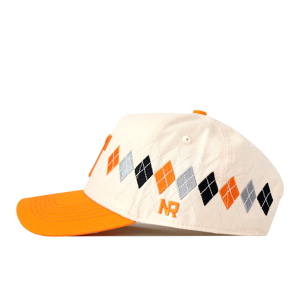Introducing the Tennessee Argyle Hat by No Rivals—a cream-colored baseball cap featuring an orange brim and crafted from a high-quality cotton blend for long-lasting comfort. This stylish snapback showcases an argyle pattern in orange, black, and gray on the side, with the embroidered NR logo in orange near the adjustable strap.