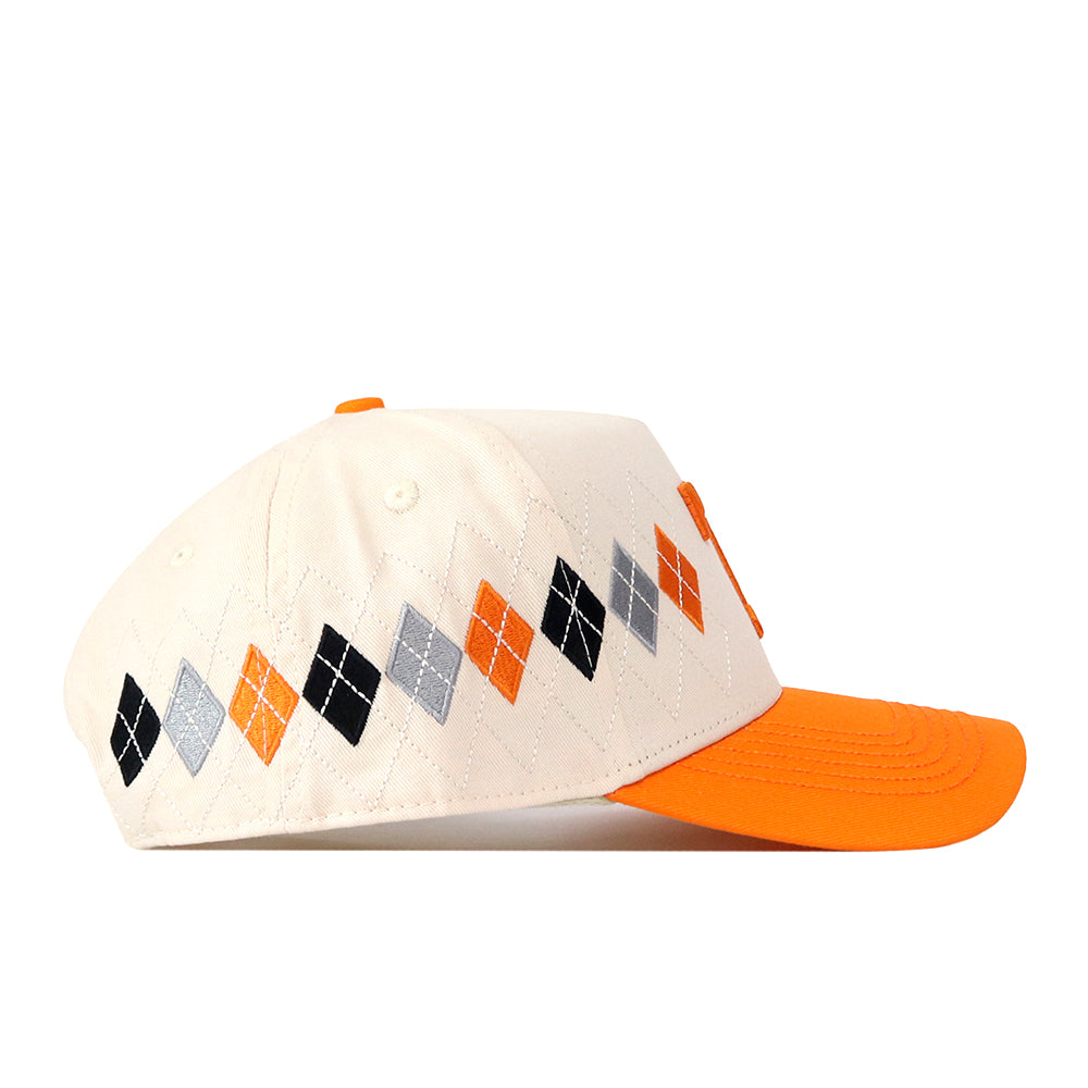 Introducing the Tennessee Argyle Hat by No Rivals—a stylish beige baseball cap with an orange brim and a distinctive argyle pattern in black, gray, and orange along the side. Made from a high-quality cotton blend, this cap features a convenient snap back closure for an adjustable and comfortable fit.