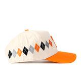 Introducing the Tennessee Argyle Hat by No Rivals—a stylish beige baseball cap with an orange brim and a distinctive argyle pattern in black, gray, and orange along the side. Made from a high-quality cotton blend, this cap features a convenient snap back closure for an adjustable and comfortable fit.