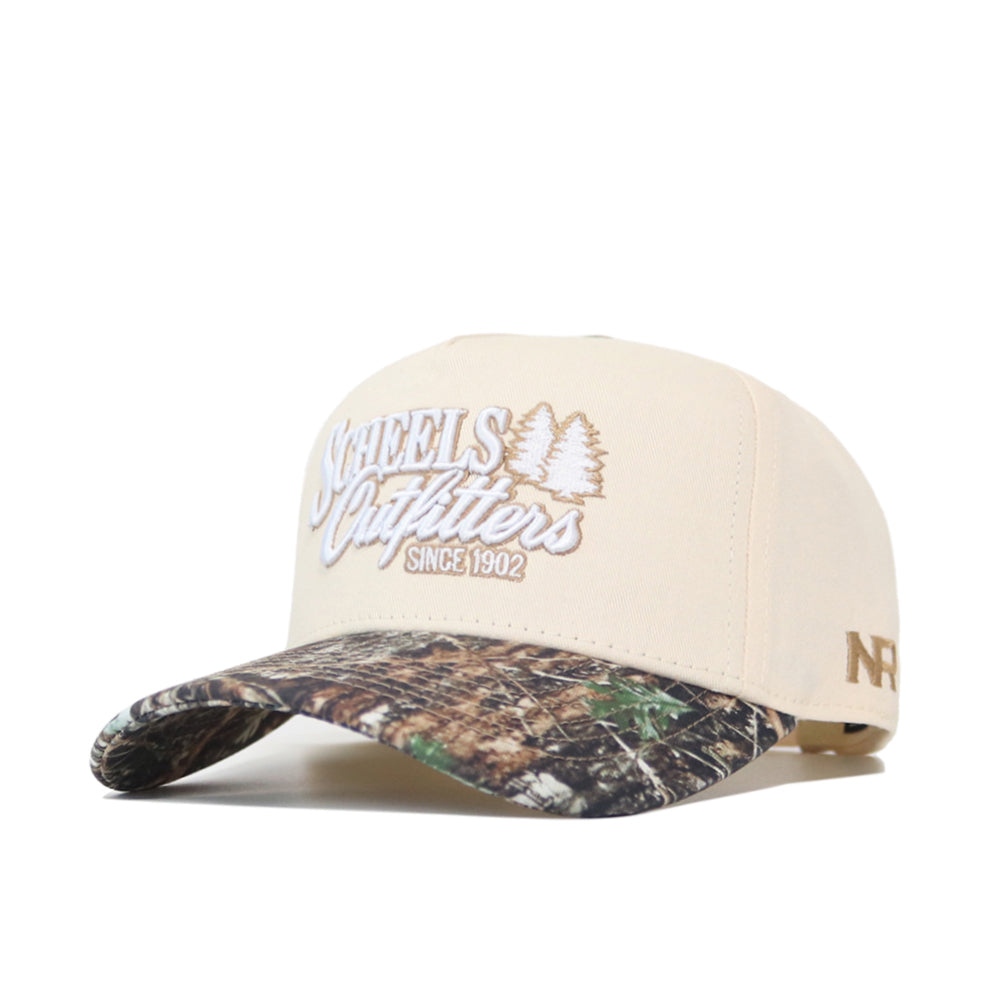 The Scheels Camo Connector Hat is a beige snapback cap with “SCHEELS Outfitters SINCE 1902” and two trees embroidered on the front, a camouflage brim, “NFR” stitched on the left side, and crafted from high-quality cotton.