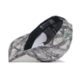 The Illinois Outland Hat by No Rivals is a structured snapback featuring green and brown woodland camo. Shown upside down, it reveals black seams, white tags, and a partially visible QR code near the back interior.