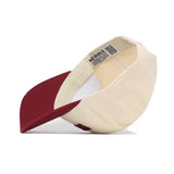 The Missoula Hometown Hat by No Rivals features a cream-colored snapback design with a maroon brim, shown angled to reveal the inside and signature NO RIVALS label. Made from high quality cotton for lasting comfort and durability.