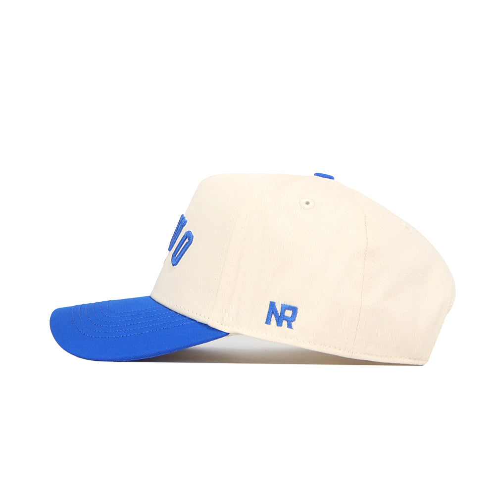 The No Rivals Provo Hometown Hat is a structured-fit beige cap with a royal blue brim and blue embroidered NR on the side. Made from durable cotton, this snapback offers lasting comfort and classic style.