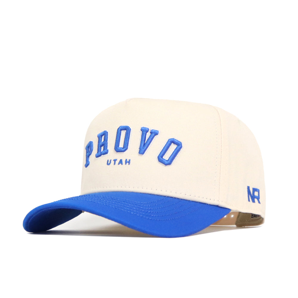 The Provo Hometown Hat by No Rivals is a cream snapback with a blue brim, raised blue "PROVO" lettering on the front, "UTAH" below, and "NR" initials in blue on the side.