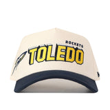 Introducing the No Rivals Toledo Alma Mater Hat—a white and navy cap featuring officially licensed embroidered Toledo Rockets logos for an authentic look, bold yellow and black “TOLEDO ROCKETS” lettering on the front, and a small rocket graphic on the side.