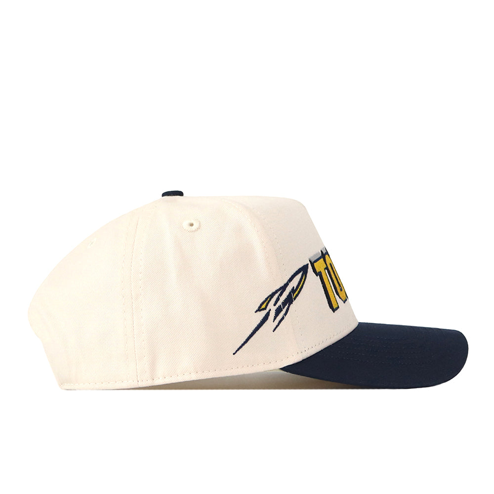 The No Rivals Toledo Alma Mater Hat is a cream-colored baseball cap with a navy blue bill, featuring embroidered logos and text on the side. This officially licensed hat also offers a convenient snap back adjustment for a comfortable fit.