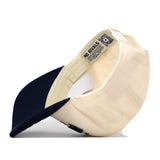 A beige and navy blue Montana State Rally Hat by No Rivals is turned inside out, revealing an inner label with text and a QR code. This officially licensed snapback cap showcases quality construction that stands out whether you wear it or put it on display.