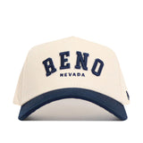 The No Rivals Reno Hometown Hat is a beige snapback with a structured fit and dark blue brim. "RENO" appears in large blue letters on the front, with "NEVADA" underneath, all crafted from comfortable cotton fabric.
