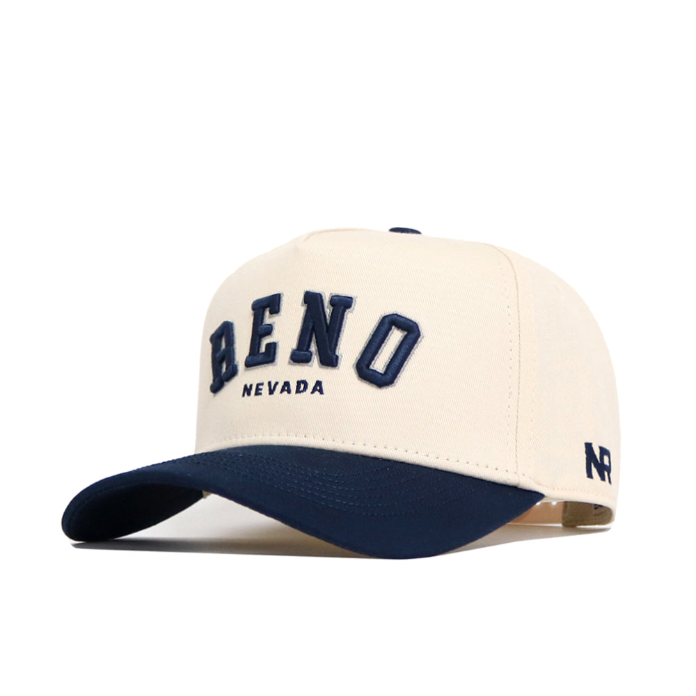 The No Rivals Reno Hometown Hat is a beige cotton baseball cap with "RENO NEVADA" embroidered in navy on the front, NR initials stitched near the brim, a structured fit, and a classic navy blue curved brim.