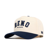 The No Rivals Reno Hometown Hat is a beige cotton baseball cap with "RENO NEVADA" embroidered in navy on the front, NR initials stitched near the brim, a structured fit, and a classic navy blue curved brim.