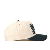 The No Rivals Michigan State Spartans Stride Hat is a cream-colored, structured fit cap with a dark green curved brim, made from high-quality cotton and featuring a partially visible graphic logo on the front. The hat is photographed against a plain white background.