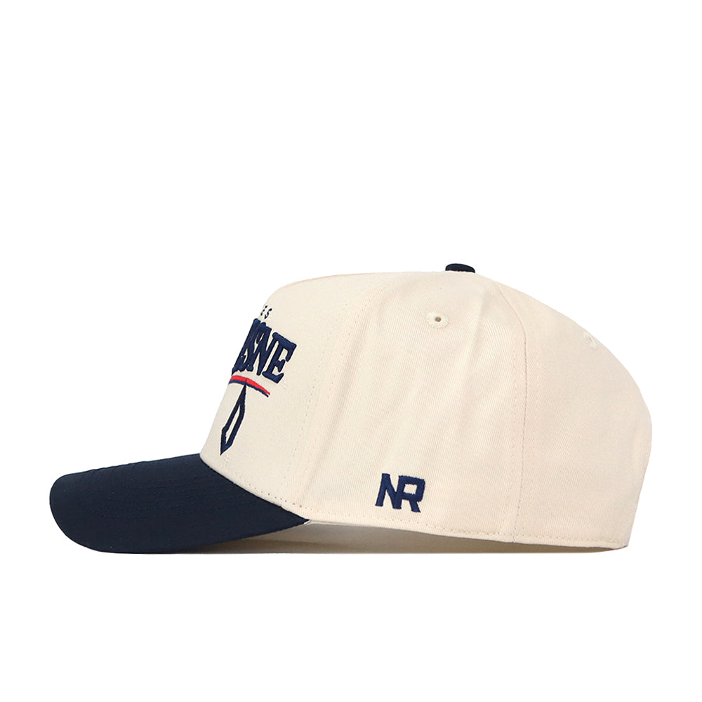 Introducing the Duquesne Stride Hat by No Rivals—a beige baseball cap with a navy brim, adorned with embroidered logos, including side embroidery that reads “NR,” and front text in striking blue and red. The snap back closure ensures an adjustable, comfortable fit.