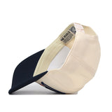 A cream and navy blue Duquesne Stride Hat by No Rivals is propped on its side, displaying the inside label, inner stitching, and adjustable snapback strap at the back.