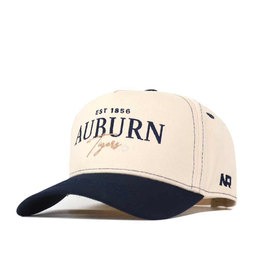 Introducing the Auburn Tigers Vintage Hat by No Rivals—a beige and navy snapback cap featuring the Auburn Tigers and EST 1856 embroidered logo on the front, with AUB letters stitched on the side. This officially licensed hat is perfect for showing off your team pride.