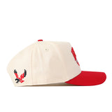 The No Rivals EWU Eagles Stadium Hat is a cream baseball cap with a red brim, highlighted by an embroidered red and black eagle logo on the left side. Made from performance fabric, it features two small side eyelets for ventilation and an adjustable snap back hat closure.