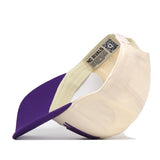 A cream and purple Kansas State Wildcats Stride Hat by No Rivals is displayed on its side, showcasing the vibrant purple underside of the brim and an inside tag with the brand’s NO RIVALS logo alongside a QR code. Perfect for your gameday fit, this snapback cap features bold embroidered Kansas State logos for a standout look.