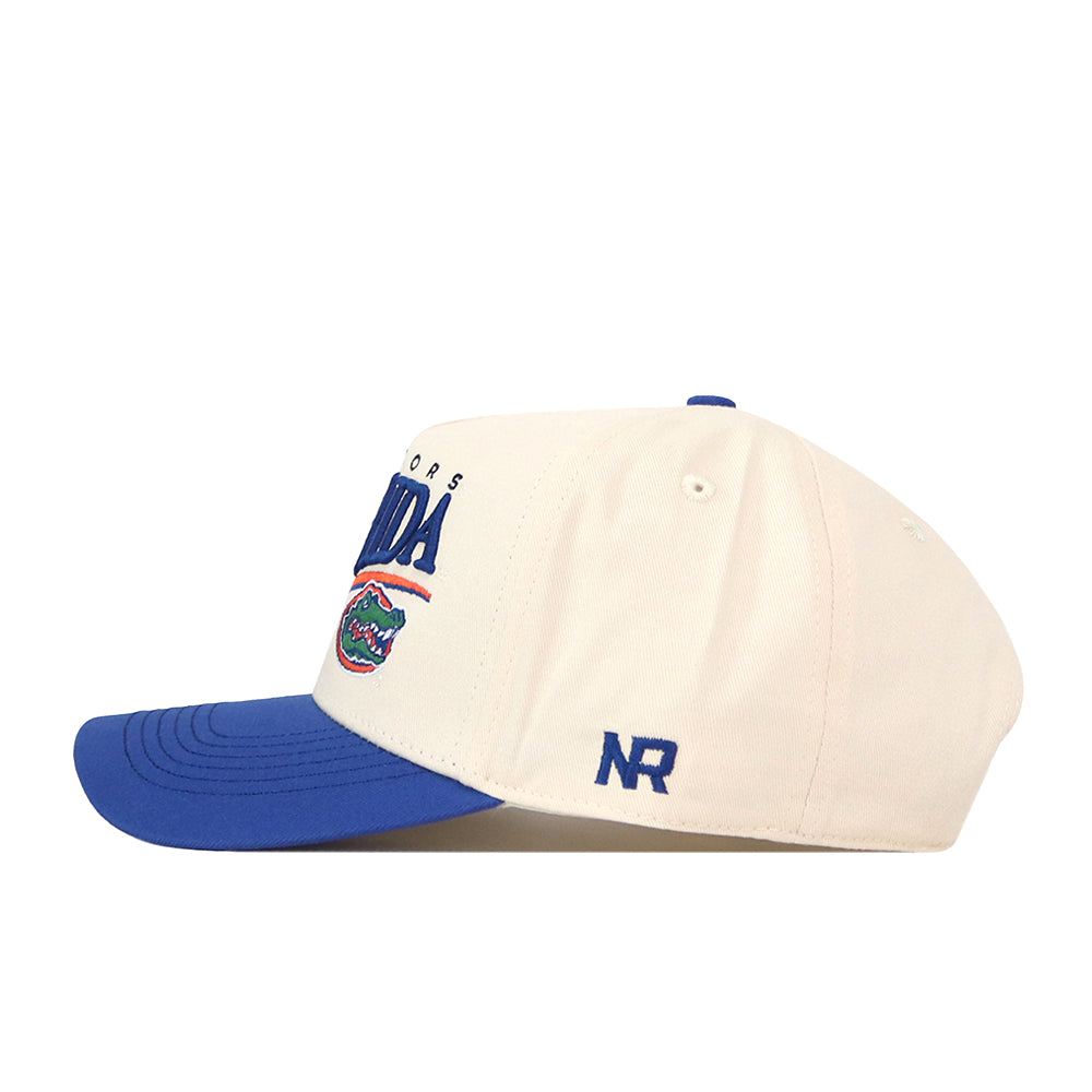 The No Rivals Florida Gators Stride Hat features a white design with a blue brim, showcasing Florida Gators text and the alligator logo on the front. Made from high-quality cotton, this structured cap provides lasting comfort. The embroidered “NR” initials appear on the side, while a snap back closure allows for adjustable fit.