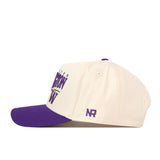 A cream-colored Washington Huskies Stride Hat by No Rivals, featuring a purple brim and a purple NR embroidered logo on the side, is shown in a side view. This stylish snapback cap adds the perfect touch to any casual outfit.