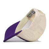 The Washington Huskies Stride Hat by No Rivals is shown upside down, displaying its interior label and QR code tag. This snap back cap features a purple brim with a cream-colored crown, and includes officially licensed embroidered logos for an authentic touch.