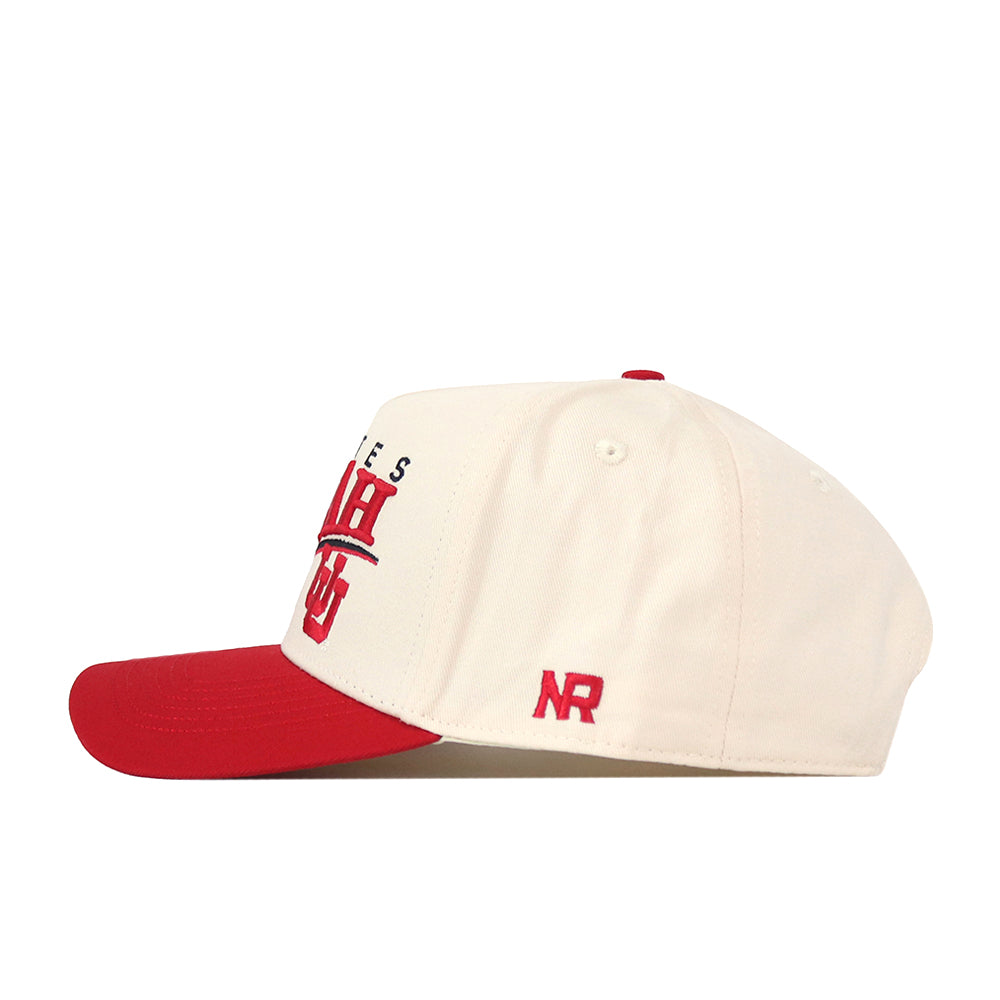 A side profile view of the Utah Utes Stride Hat by No Rivals, a cream-colored, officially licensed baseball cap featuring a red brim, red embroidered lettering on the front, and “NR” stitched in red on the side.