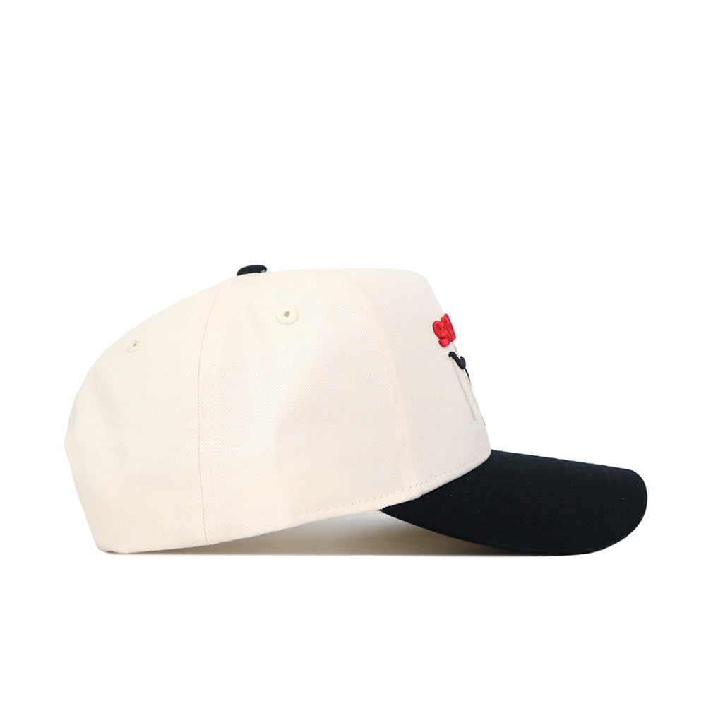 The Scheels Longhorn Hat - Black is a cream baseball cap with a black brim, shown from the side on a white background. Made of high-quality cotton, this structured snapback features red and black embroidery on the front.